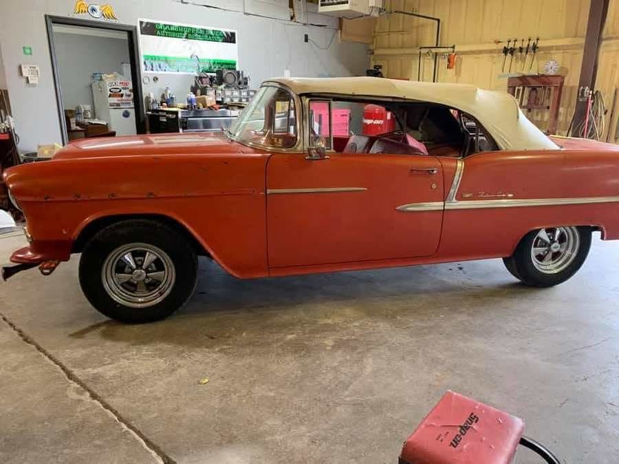 Red 1955 Chevrolet convertible with white top inside the shop