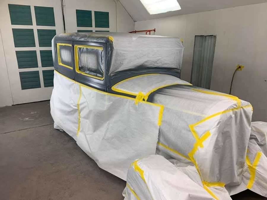 Car masked in the paint booth, paper and yellow tape covering everything but the body line